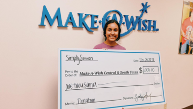 Simran holding a big check make out to Make-A-Wish CSTX for $1,000