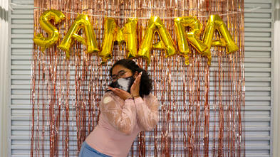 Wish kid Samara posing and smiling in front of gold balloons that spell out "Samara"