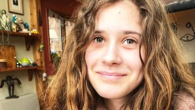 A young woman with wavy brown hair smiles