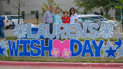 Lauren and her family standing in front of a yard sign that says "Lauren's Wish Day"