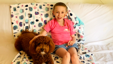 Wish kid Eleanor sitting on her bed with her goldendoodle puppy, Willow.