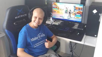 Tiago, age 15, in blue Make-A-Wish shirt, in front of new gaming computer set-up