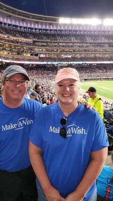 Jon and Vicki at a Twins baseball game wearing their Make-A-Wish shirts and smiling.