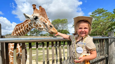wish kid Amelia dressed in a zoo keeper feeding a giraffe
