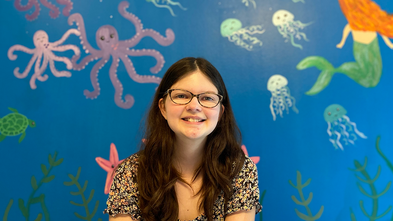 Addison smiles in front of a hospital wall that she painted