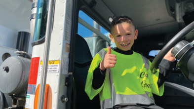 Carter sits in the garbage truck, giving a thumbs up