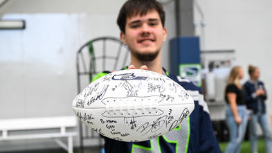 Wish kid Keegan holding signed football toward camera 