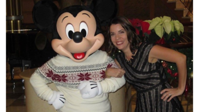 Molly poses on the right arm and arm with Mickey Mouse wearing a holiday sweater. Molly is wearing a black lace dress. Molly has short brown hair. 