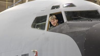 Isaiah peeking out the cockpit window, smiling. The picture is taken from outside the plane. 