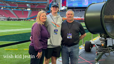 Wish kid Jestin with his parents, standing on a football stadium on the sidelines.