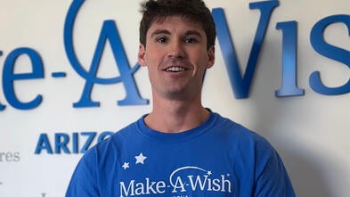 Ben Posorske stands in front of the Make-A-Wish Arizona wish wall.