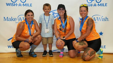 A young wish boy smiling with three Wish-A-Mile women riders