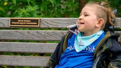 Derek sitting on his donated bench smiling with a plaque to honor him