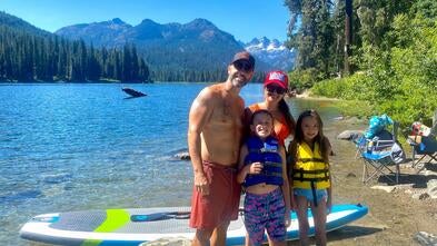 Family in swimming gear next to a boat by the water and the sun is shining. 