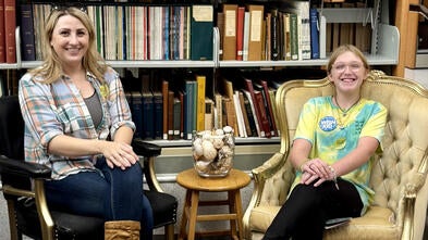 Neveah and Shannon sitting together in front of books.