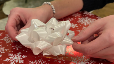 The hands of wish kid Emma, adding a bow to a wrapped holiday gift