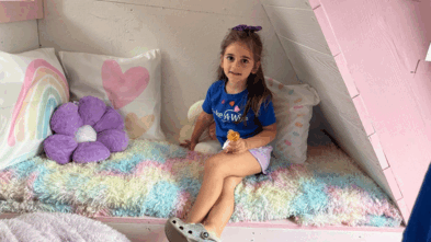 Tessa on a bench in her playhouse holding a doll