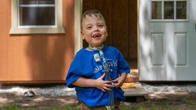 boy wearing blue Make-A-Wish shirt outside his playhouse