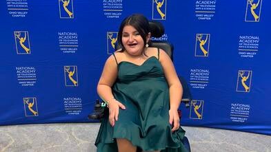 A photo of wish kid Addie in fancy dress smiling in front of a backdrop at an awards gala.
