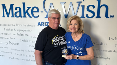 Pat and Bill Clemency standing by the Wish Wall smiling