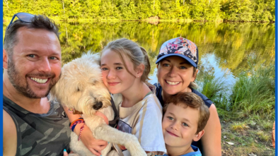 Teresa with her son, daughter, husband, and dog smiling in front of a lake