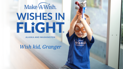 Wish kid Granger holding a toy plane. Logo for Make-A-Wish Alaska & Washington Wishes in Flight overlayed on the background of the image
