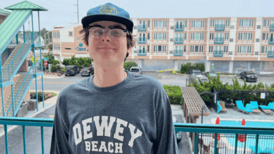 Aidan standing on a porch wearing a shirt that says "Dewey Beach"