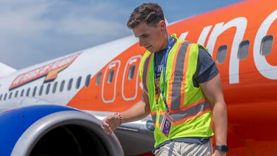 Jared in a safety vest walking out of a Sun Country Airline plane