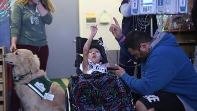 Neeno in a wheelchair at his birthday party wish, surrounded by his dad, a service dog, and a nurse