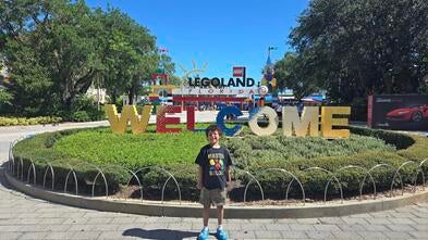 A young boy standing in front of Legoland smiling