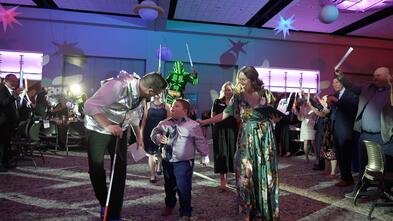 A visually impaired boy is being walked down the aisle to enter the stage where he will find out his wish is coming true!