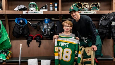 Cameron holding up a custom jersey next to Marc Fleury in the Wild locker room