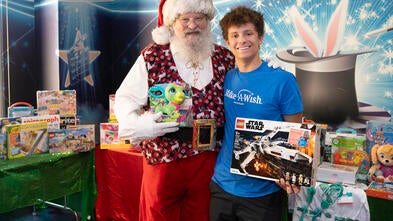 A teenage boy standing with Santa, holding presents for other children