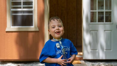 Axle standing in front of his new playhouse. He is smiling and holding his breathing tube.