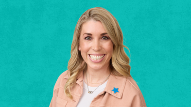 A woman with blonde hair smiles broadly at the camera, wearing a light pink denim jacket over a white t-shirt. A blue star-shaped pin is visible on her jacket. The background is a textured teal color.