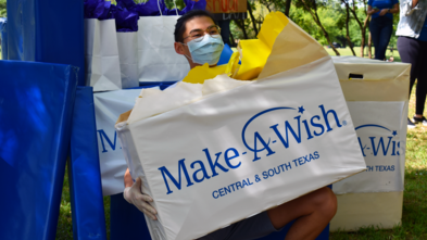 Wish Kid Joshua holding his present and smiling (under a mask)