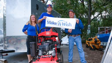 Wish Kid Mason standing on his brand new lawnmower with his mom and a Gravely employee