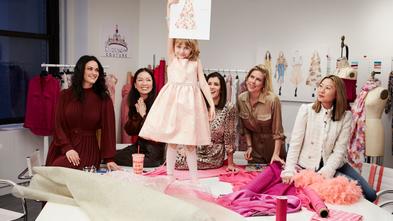 Wish Kid Elizabeth holding up her dress design while the designers smile up at her.