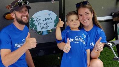 Grayson and his parents give a thumbs up in front of his new camper.