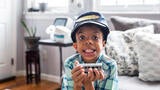 Wish kid Hazael sitting in living room holding toy train with conductor's hat on head