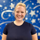 Stefanie in a black shirt in front of a blue wall with silver stars