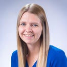 Woman smiling with long blonde hair. She is wearing a bright blue long sleeve shirt.
