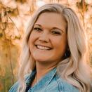 Karissa has long blonde hair and wears a jean jacket. She is smiling and standing in a field.