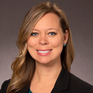 A woman smiling with shoulder length blonde hair. She is wearing a blazer and a teal blouse.