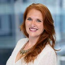 Woman with long red hair. She is wearing a white blouse 