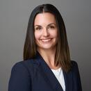 Melissa in a navy blazer posing in front of a gray background