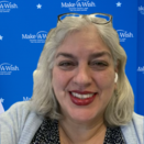 Lillian stands in front of Make-A-Wish wall
