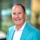 A man with short dark hair, wearing a teal jacket with white shirt.