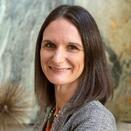 Headshot of Melissa wearing a gray blazer in front of a blurred background