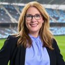 Head shot of Sara in a blue shirt and black blazer with Allianz Field blurred behind her